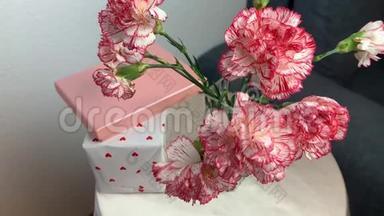 一束粉红色的康乃馨花放在花瓶里，盒子里的礼物放在一张灰色沙发旁边的圆桌上，甜蜜的概念